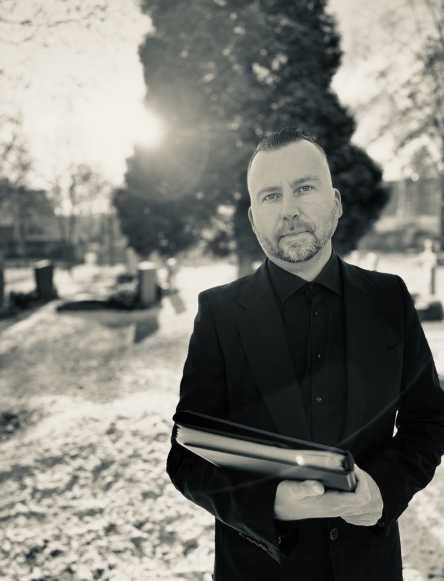 Thomas Meyer, Trauerredner, mit Redemappe auf einem Friedhof